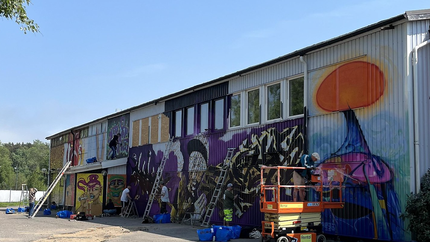 Foto på flertal graffitikonstnärer som håller på att måla en stor fasad.