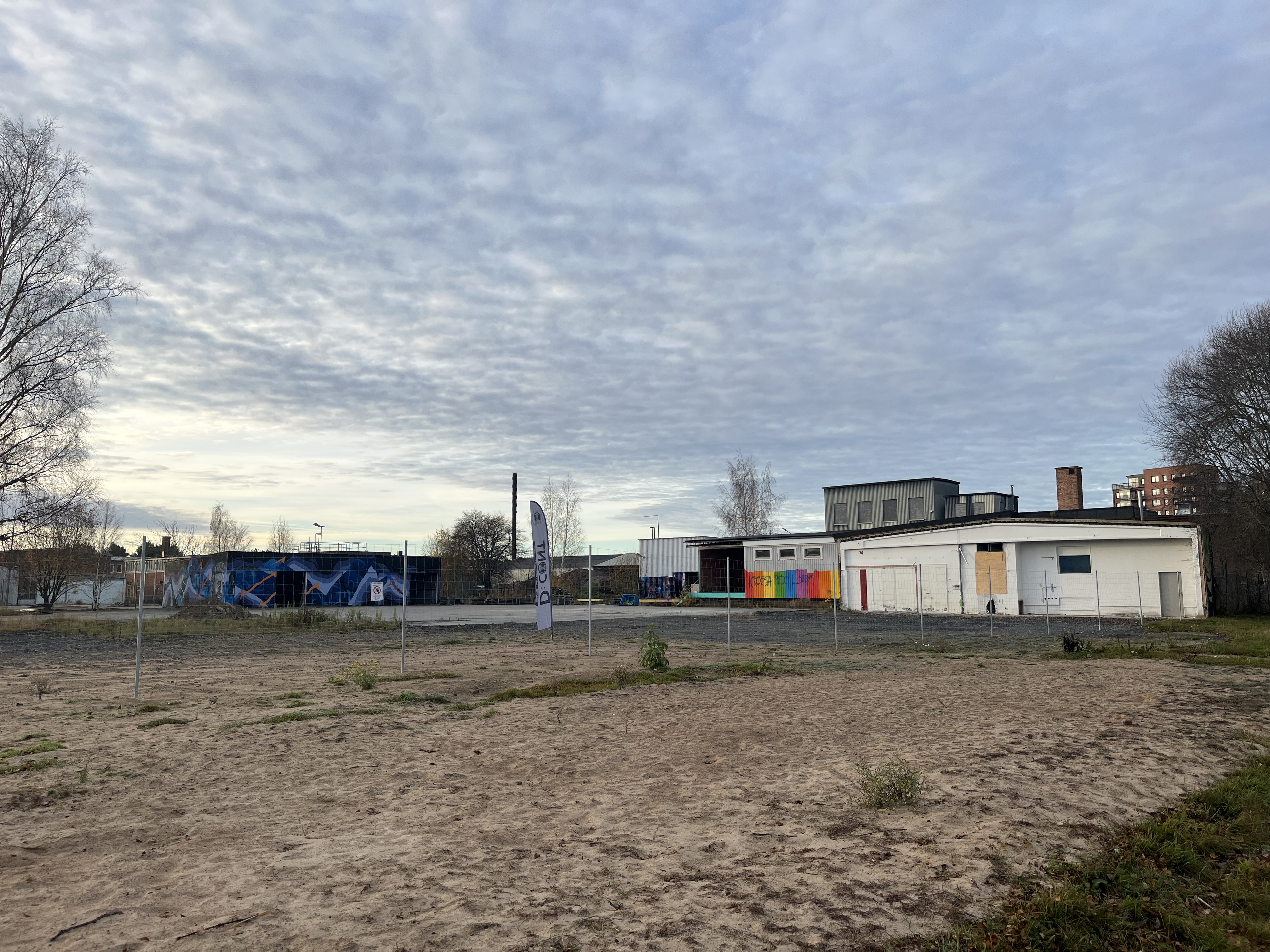 Syrgasverkets baksida. Bredvid står två stora plåtskjul med graffitimålning på.