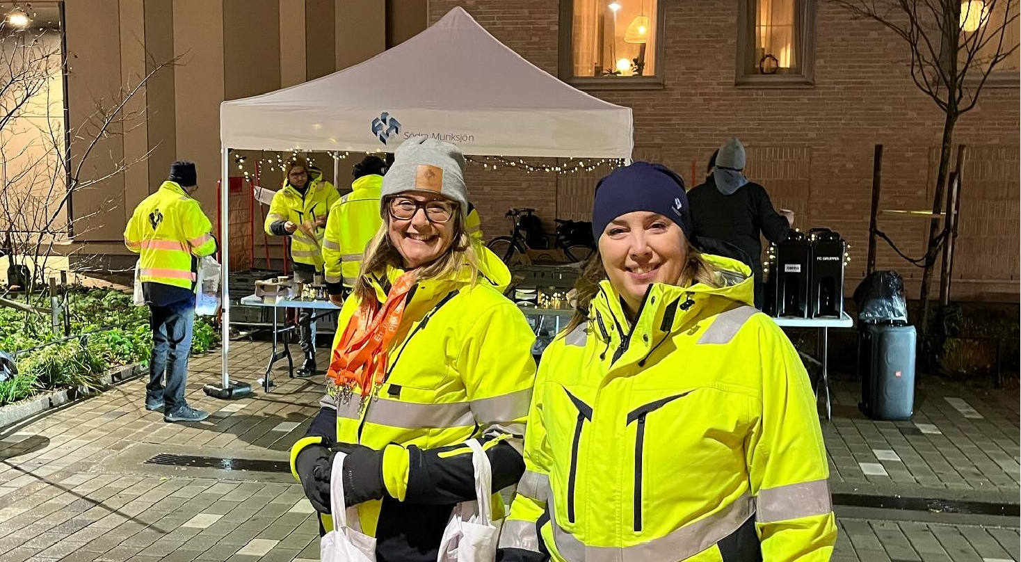 Flera personer i varselkläder står vid ett partytält med bord fulla med fika.