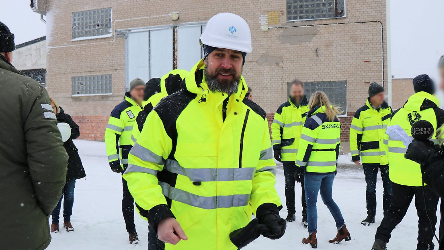 Henrik Gustafsson i varseljacka och vit hjälm. Bakom honom är flera människor med varseljackor.