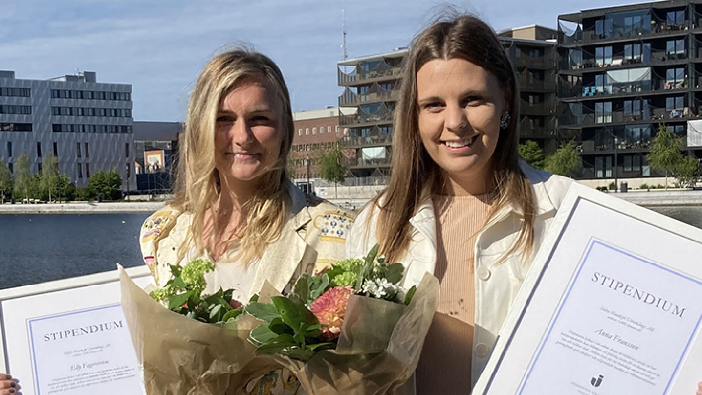 Två tjejer står framför Munksjön och håller i sina inramade stipendier och varsin bukett med blommor.