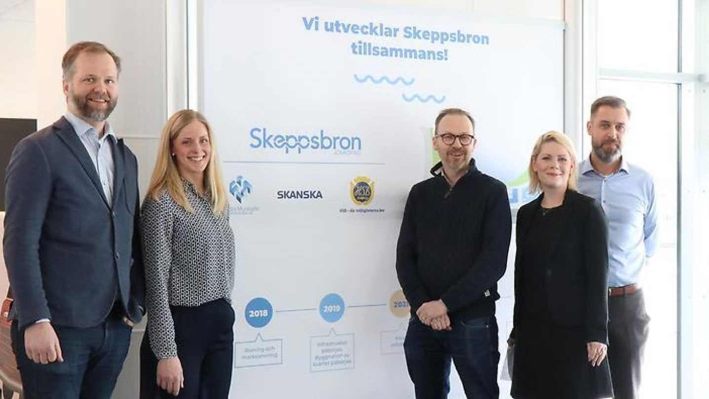 Flertalet personer står uppradade framför en skylt där det står "Vi utvecklar Skeppsbron tillsammans!".