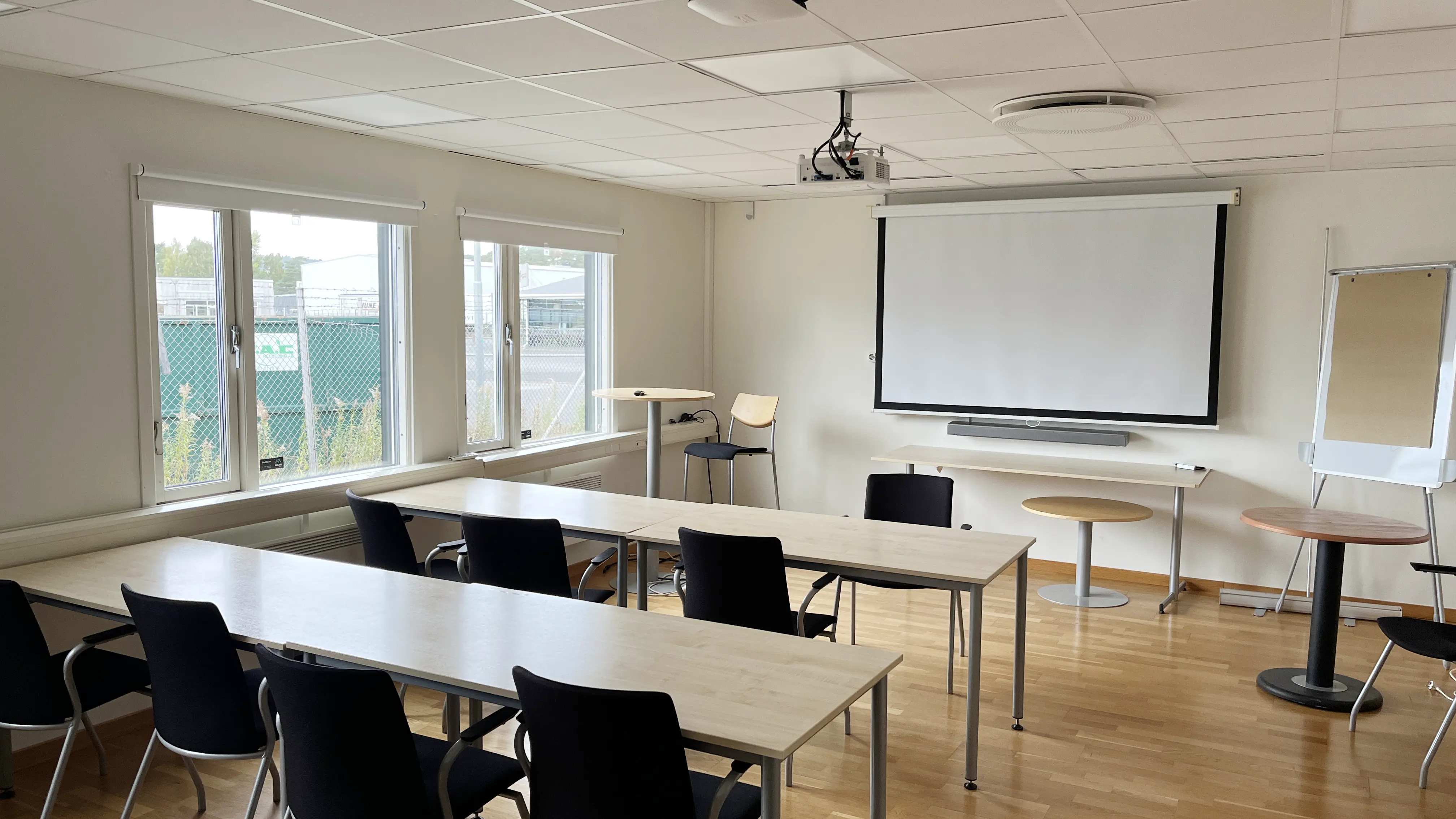 Konferensrum med bord, stolar, projektor och stor bildskärm.