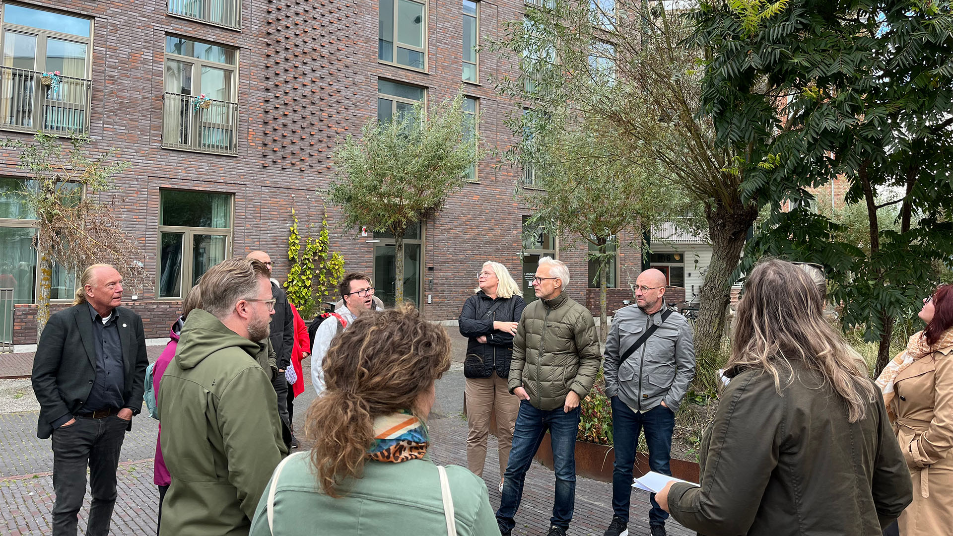 En grupp människor står i en cirkel och tittar upp mot husfasader.