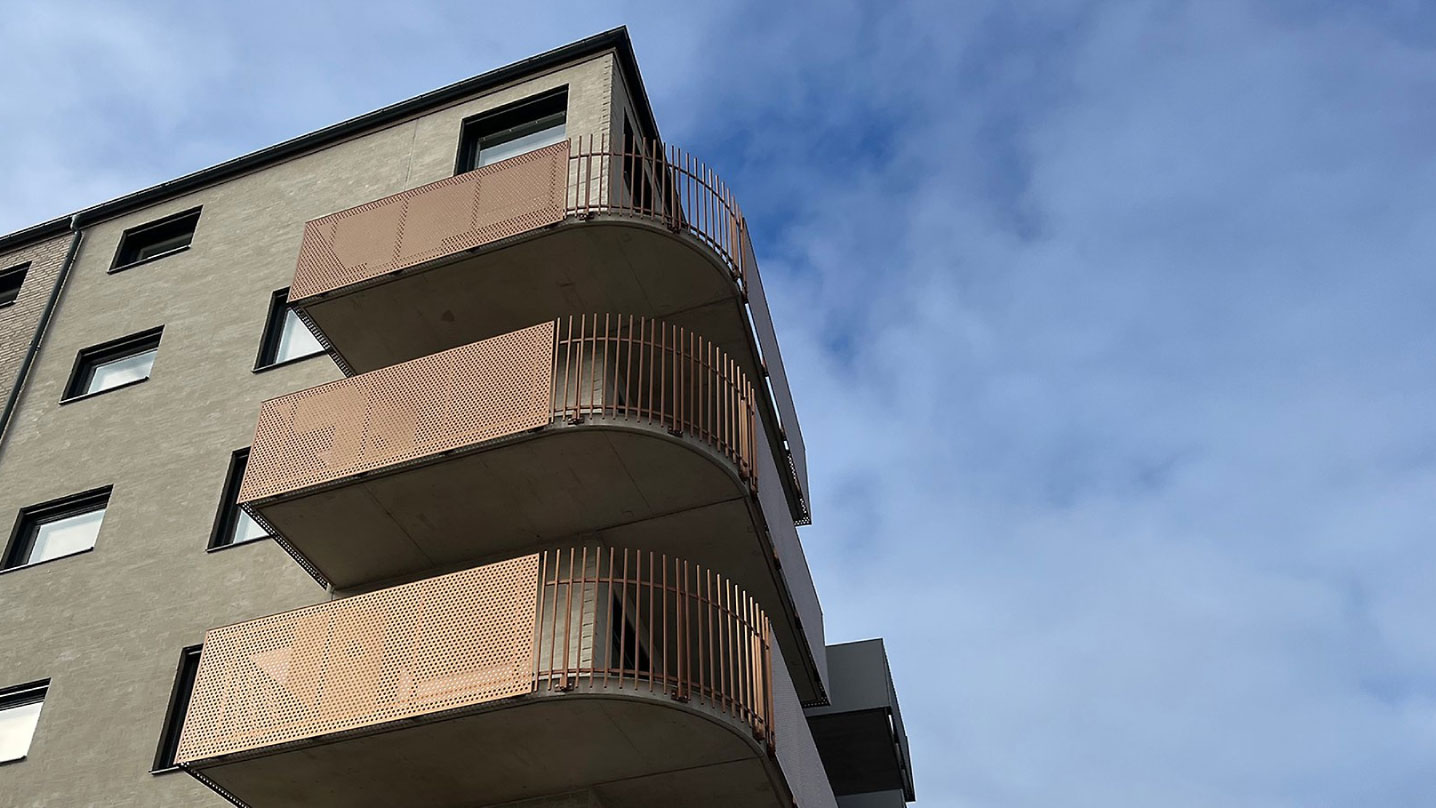 Bild tagen underifrån på tre balkonger på ett flerbostadshus. Blå himmel syns i bakgrunden.
