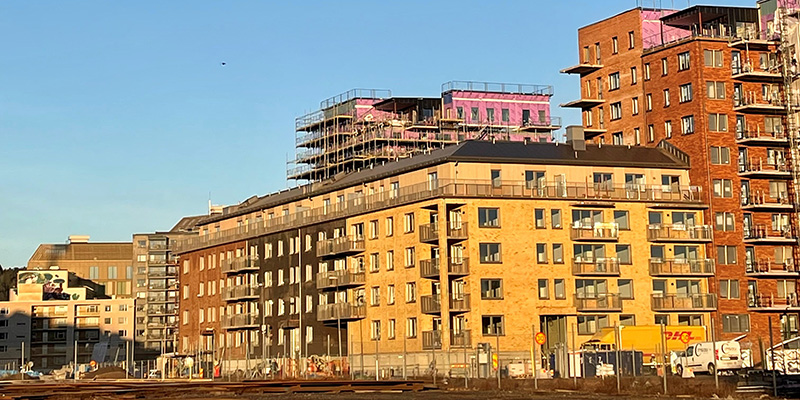 Foto på Skanskas hus, kvarter 9. Kvarteret består av två högra huskroppar i rött tegel med balkonger. Mellan husen finns ett lägre femvåningshus i gult och mörkbrunt tegel.