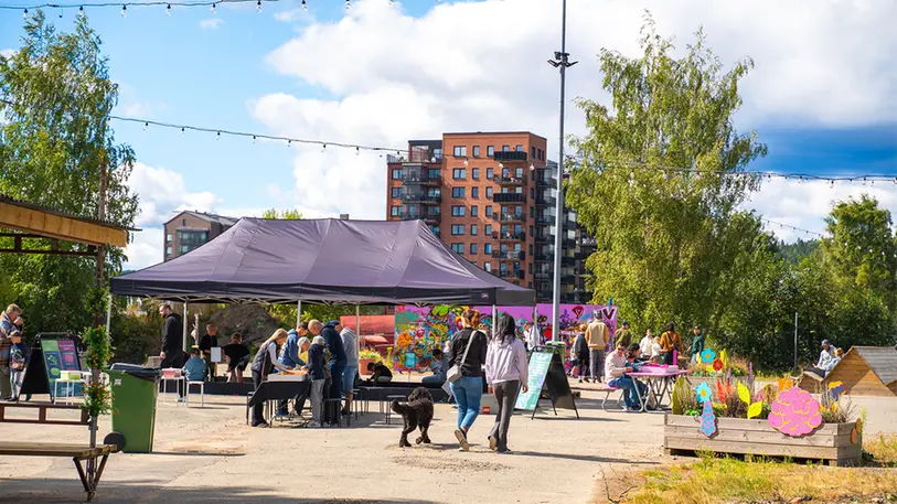 Ett torg med bänkar och partytält. I tältet bygger vuxna och barn lego. Människor rör sig på torget.