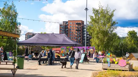 Ett torg med bänkar och partytält. I tältet bygger vuxna och barn lego. Människor rör sig på torget.