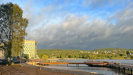 En brygga på en sjö. I bakgrunden syns en höjd med träd och hus. I förgrunden syns jord efter byggnation.