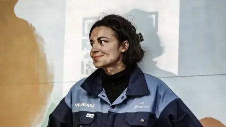 En brunhårig kvinna med blå jacka står leende.