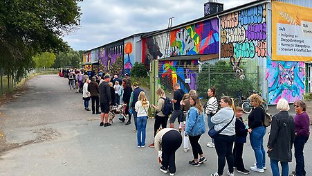 Människor står i en lång kö utanför ett hus som är målat med grafitti